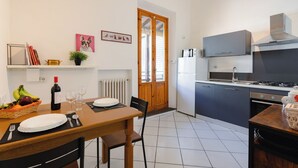 A modern kitchen with a dining area, featuring a stove, refrigerator, and a wooden dining table set for two. - Vanna's House near the center of Florence (Firenze)