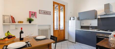 A modern kitchen with a dining area, featuring a stove, refrigerator, and a wooden dining table set for two.