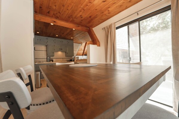 A modern kitchen with wooden beams, a large dining table, and a view of the outdoors. - Sequoia Vintage A-frame River Retreat (Three Rivers)