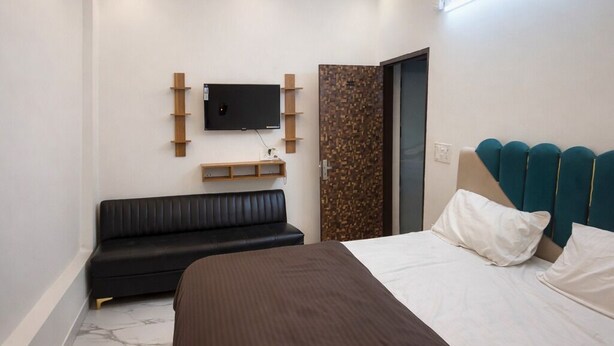 A modern bedroom with a large bed, a ceiling fan, recessed lighting, a TV, and a built-in bench. - Roomshala Hotel Scorpio (New Delhi)