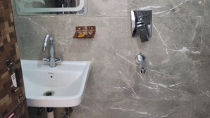 A bathroom with a white sink, a mirror, a soap dish, and a showerhead. - Roomshala Hotel Scorpio (New Delhi)