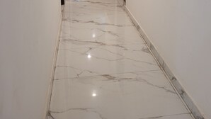 A hallway with a marble floor, a black sofa, and a door on the right. - Roomshala Hotel Scorpio (New Delhi)