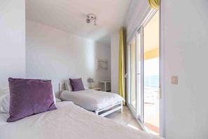 Une chambre d’hôtel avec deux lits, une table de chevet, une lampe et une vue sur la mer, accessible par une porte coulissante.