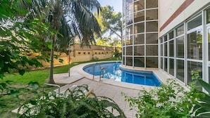 A swimming pool surrounded by a garden with palm trees and a building with large windows. - Mediterranean Beach front Apartment: Large terrace, Air Conditioning, Wi-fi, Pool. (Fuengirola)
