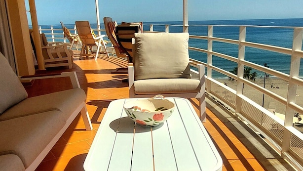 A sunlit outdoor area with a table, chairs, and a view of the ocean. - Mediterranean Beach front Apartment: Large terrace, Air Conditioning, Wi-fi, Pool. (Fuengirola)