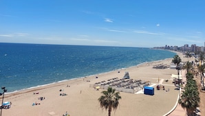 A beach with a city skyline in the background, a clear sky, and a calm sea. - Mediterranean Beach front Apartment: Large terrace, Air Conditioning, Wi-fi, Pool. (Fuengirola)