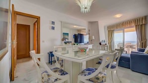 A dining area with a glass table and white chairs, a living area with a sofa and a view of the sea, and a kitchen with modern appliances. - Mediterranean Beach front Apartment: Large terrace, Air Conditioning, Wi-fi, Pool. (Fuengirola)
