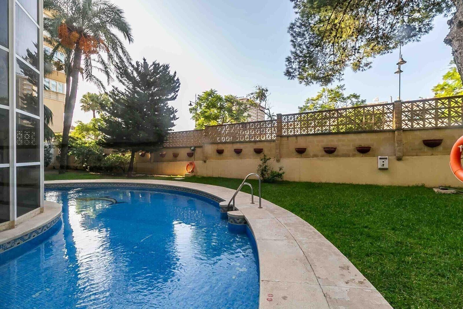 Una piscina rodeada por una cerca, césped y árboles.