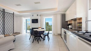 A modern kitchen with a dining area, a TV mounted on the wall, and a balcony with a view. - Thea Estate (Corfu)