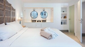 A modern hotel room with a large bed, two round mirrors above the sink, and a decorative wall panel. - Thea Estate (Corfu)