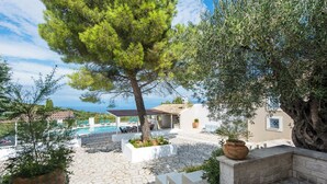 A poolside area with a stone patio, a tree, and a view of the sea. - Thea Estate (Corfu)