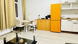 Eine kompakte Küche mit einem gelben Kühlschrank, weißen Schränken und einem Essbereich mit einem Glastisch und Stühlen.