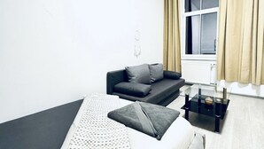 Ein modernes Wohnzimmer mit einem grauen Sofa, einem Glastisch und einem weißen Bett.