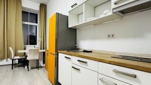 Eine moderne Küche mit weißen Schränken, einem schwarz-orangenen Kühlschrank, einer Holz Arbeitsplatte und einem Fenster mit beige farbenen Vorhängen.
