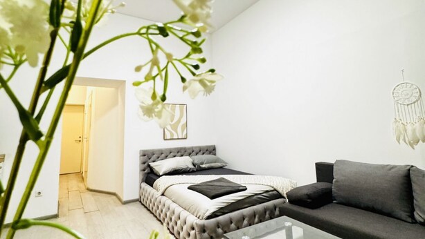 Ein modernes Schlafzimmer mit einem geblatteten Bett, einem grauen Sofa und einem Traumfänger an der Wand.