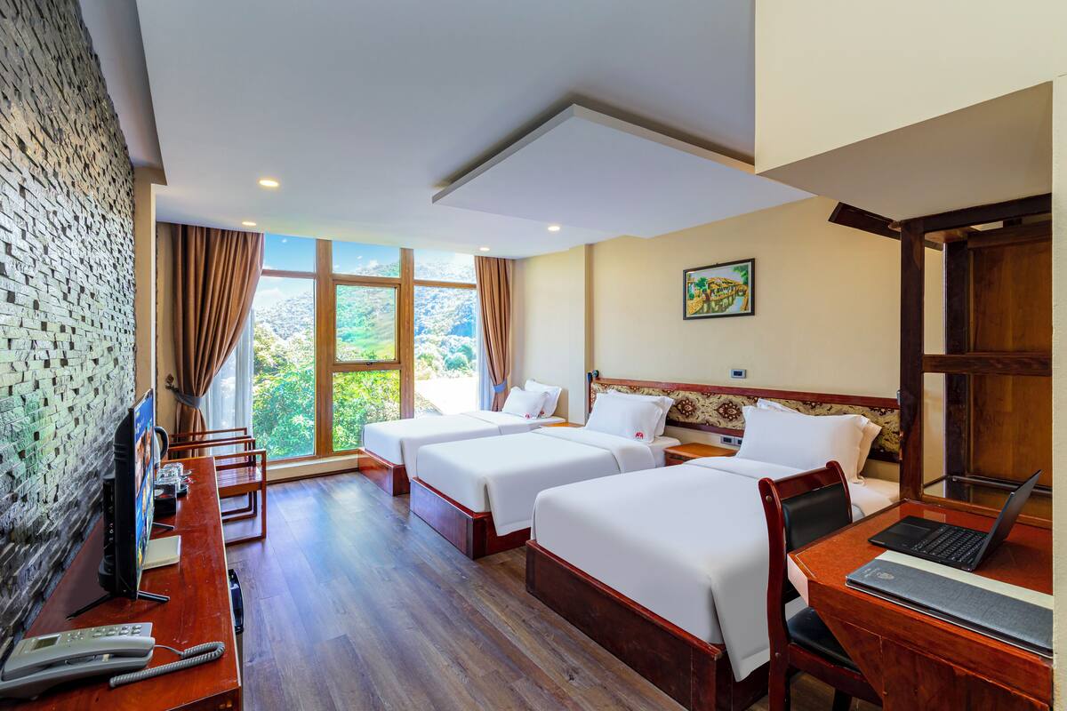 A hotel room with two beds, a desk with a laptop, a telephone, and a TV.