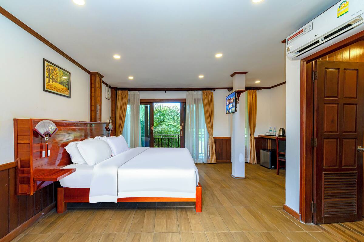A hotel room with a wooden bed, a desk, and an air conditioning unit.