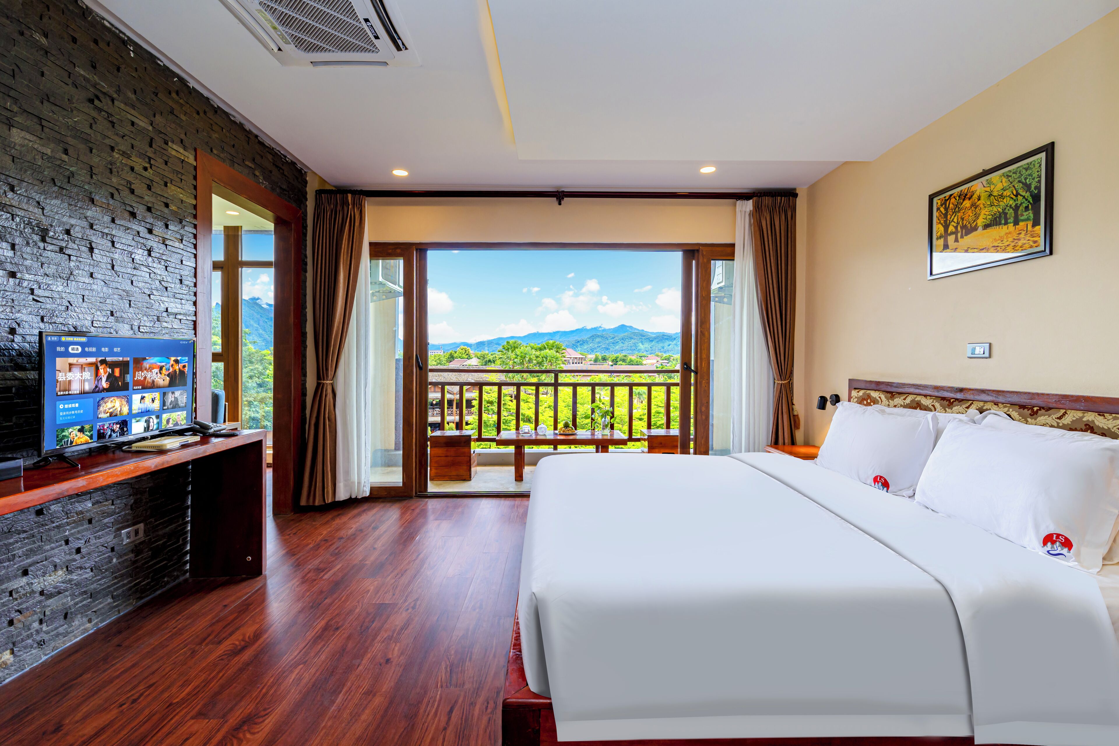 Habitación de hotel con una cama grande, un televisor sobre un mueble de madera y un balcón con vistas a las montañas.