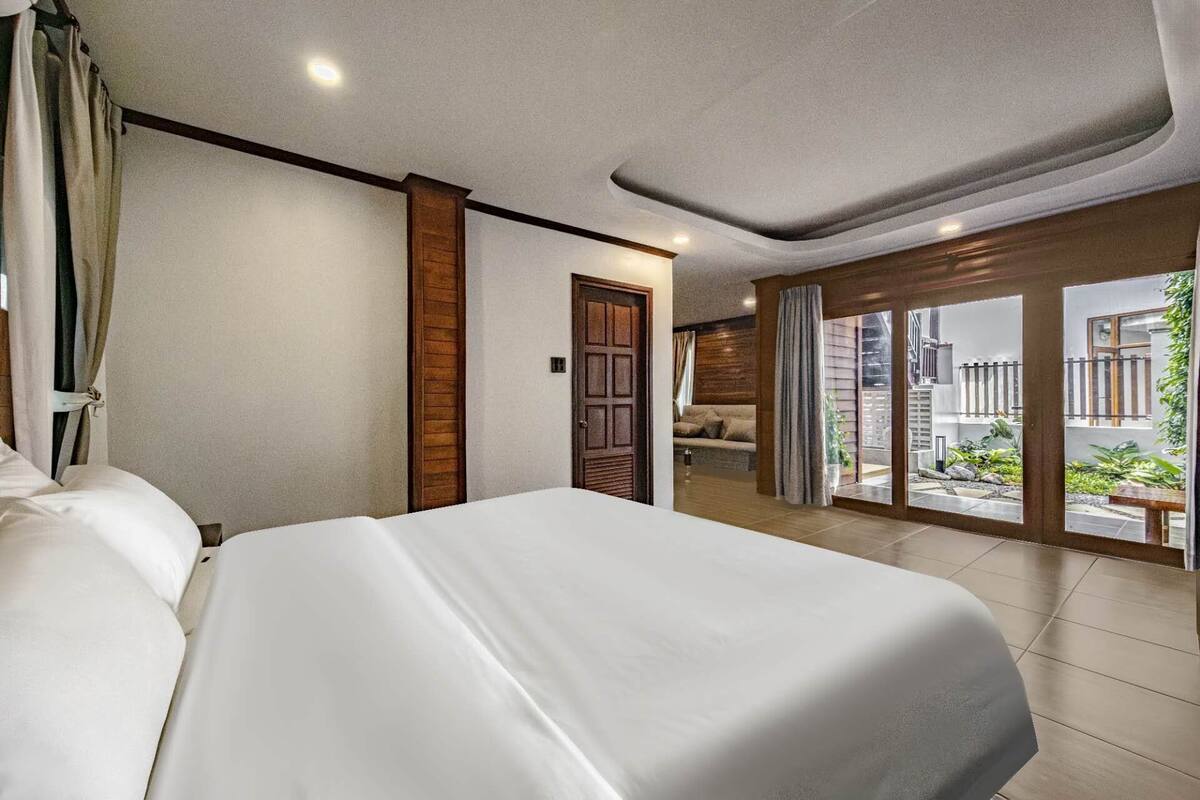 A hotel room with a large bed, a wooden door, and a view of the outdoor area through glass doors.