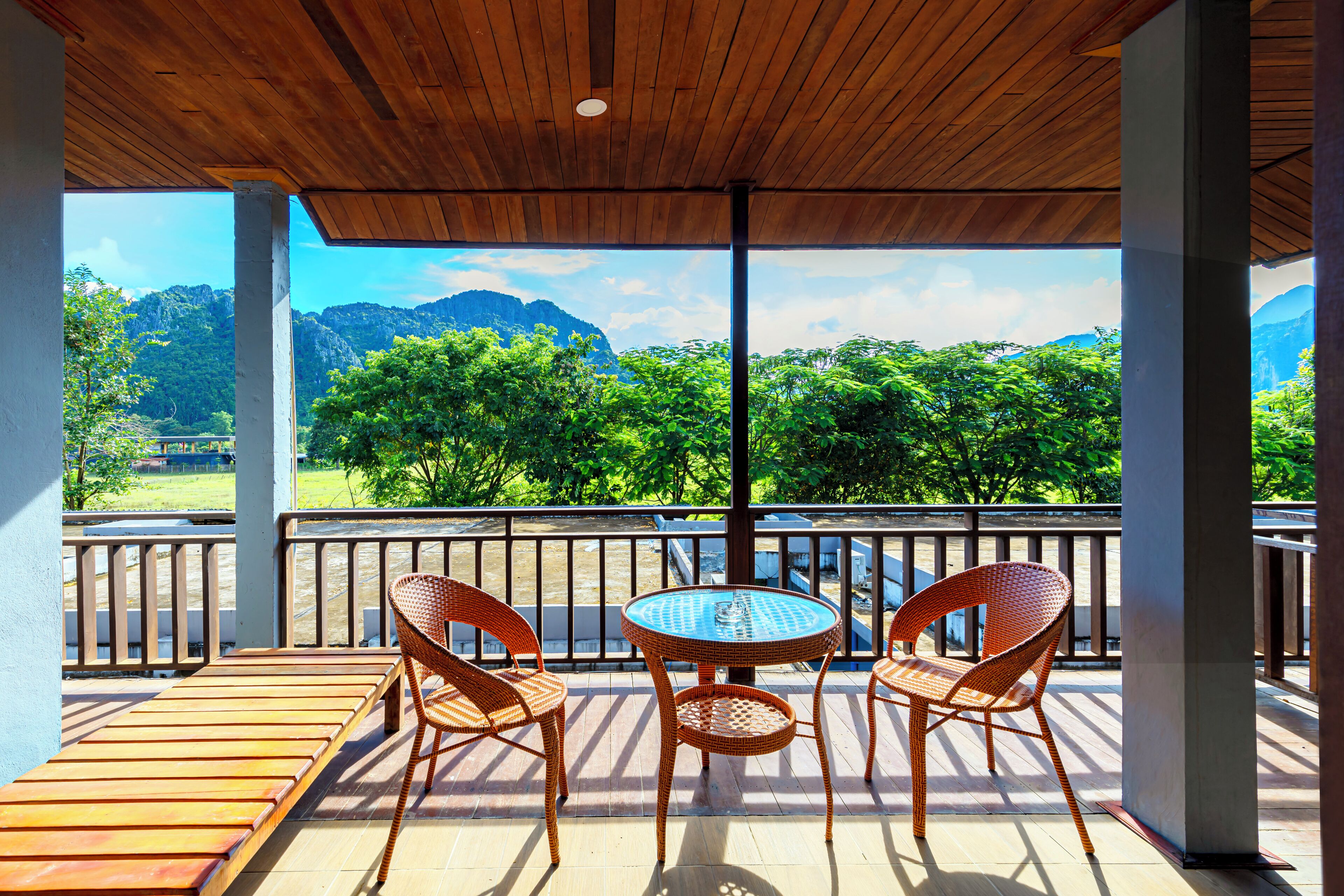 Un espacio al aire libre techado con sillas de mimbre y una mesa, con vistas a un paisaje montañoso.