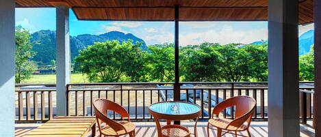 Un espacio al aire libre techado con sillas de mimbre y una mesa, con vistas a un paisaje montañoso.