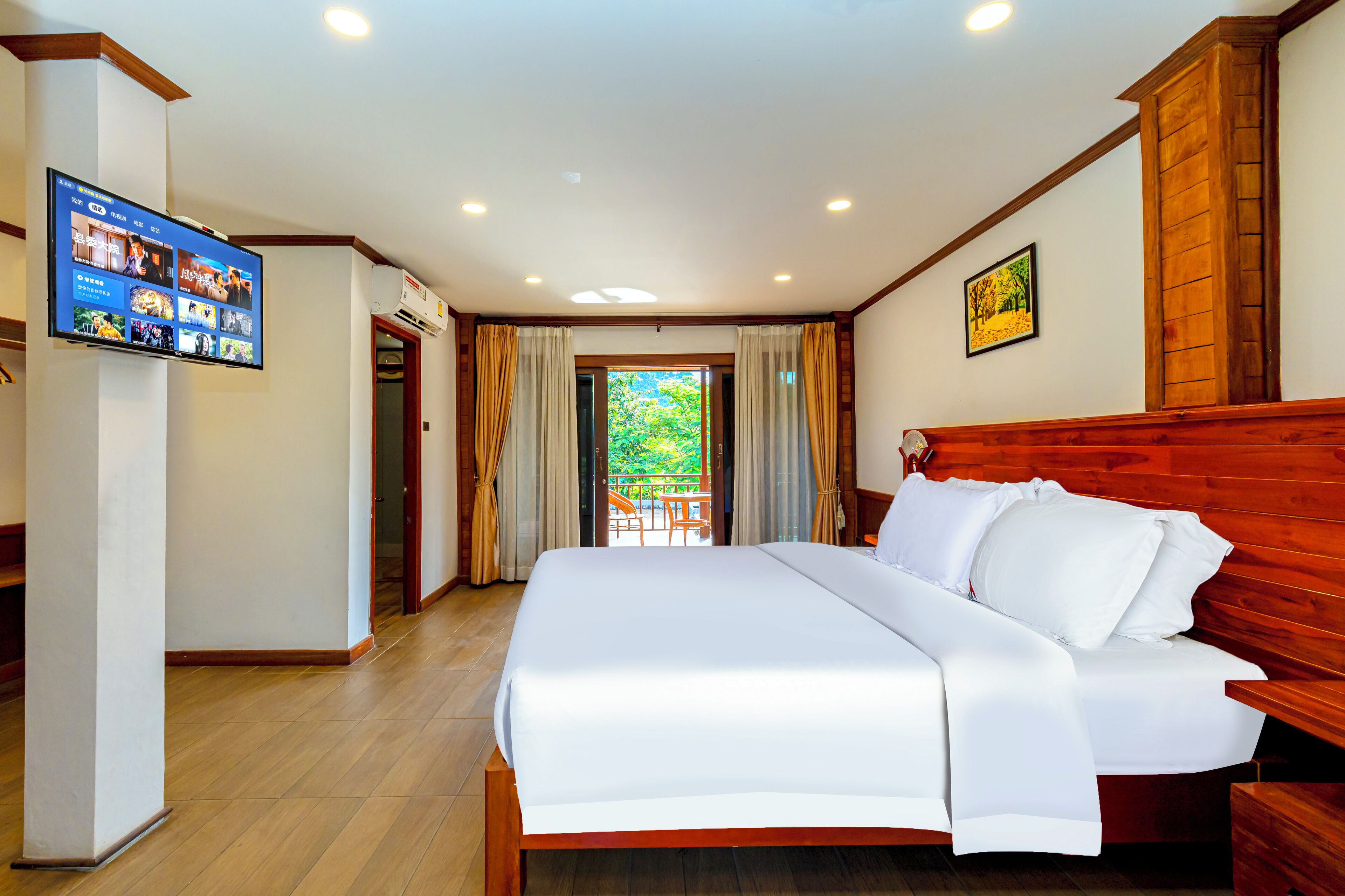 A hotel room with a large bed, wooden headboard, a flat-screen TV mounted on the wall, and a view of the outdoors through a door.