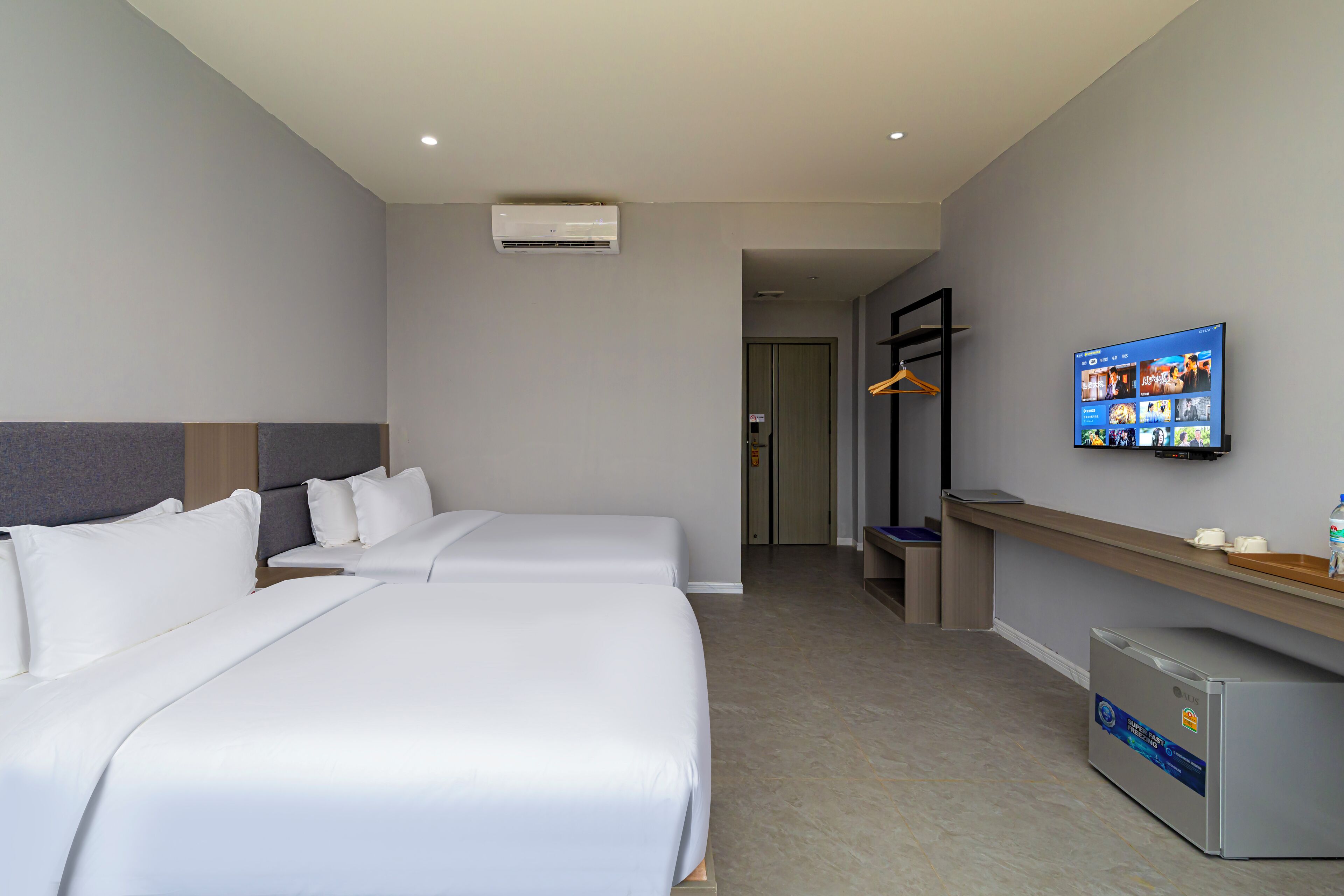 A hotel room with two beds, a TV mounted on the wall, a mini-fridge, and a coat rack.