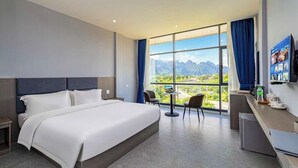 Une chambre d’hôtel moderne dotée d’un grand lit, d’un petit bureau, d’une chaise et offrant une vue sur les montagnes grâce à de grandes fenêtres.