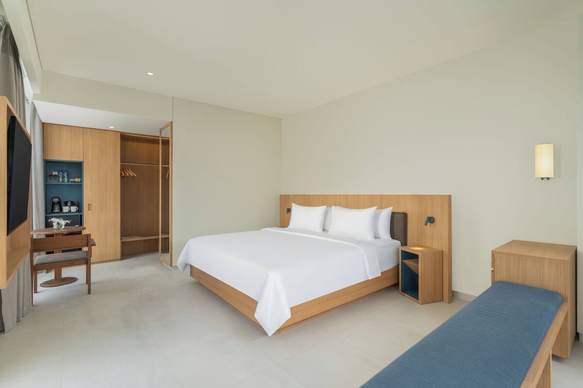 Una habitación de hotel moderna con una cama grande, mesitas de noche, un banco, un escritorio con una silla y un armario.