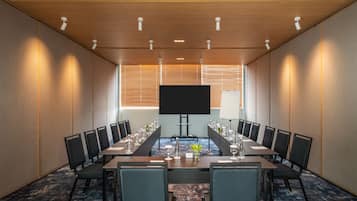 Un salón de conferencias con una larga mesa, sillas, una pantalla de televisión y una pizarra.
