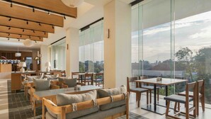 Un moderno vestíbulo de hotel con zona de comedor, ventanas amplias y vistas a la ciudad.