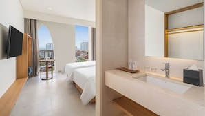 Habitación de hotel con dos camas, televisor, escritorio con silla, baño con lavamanos y espejo, y vista a la ciudad.