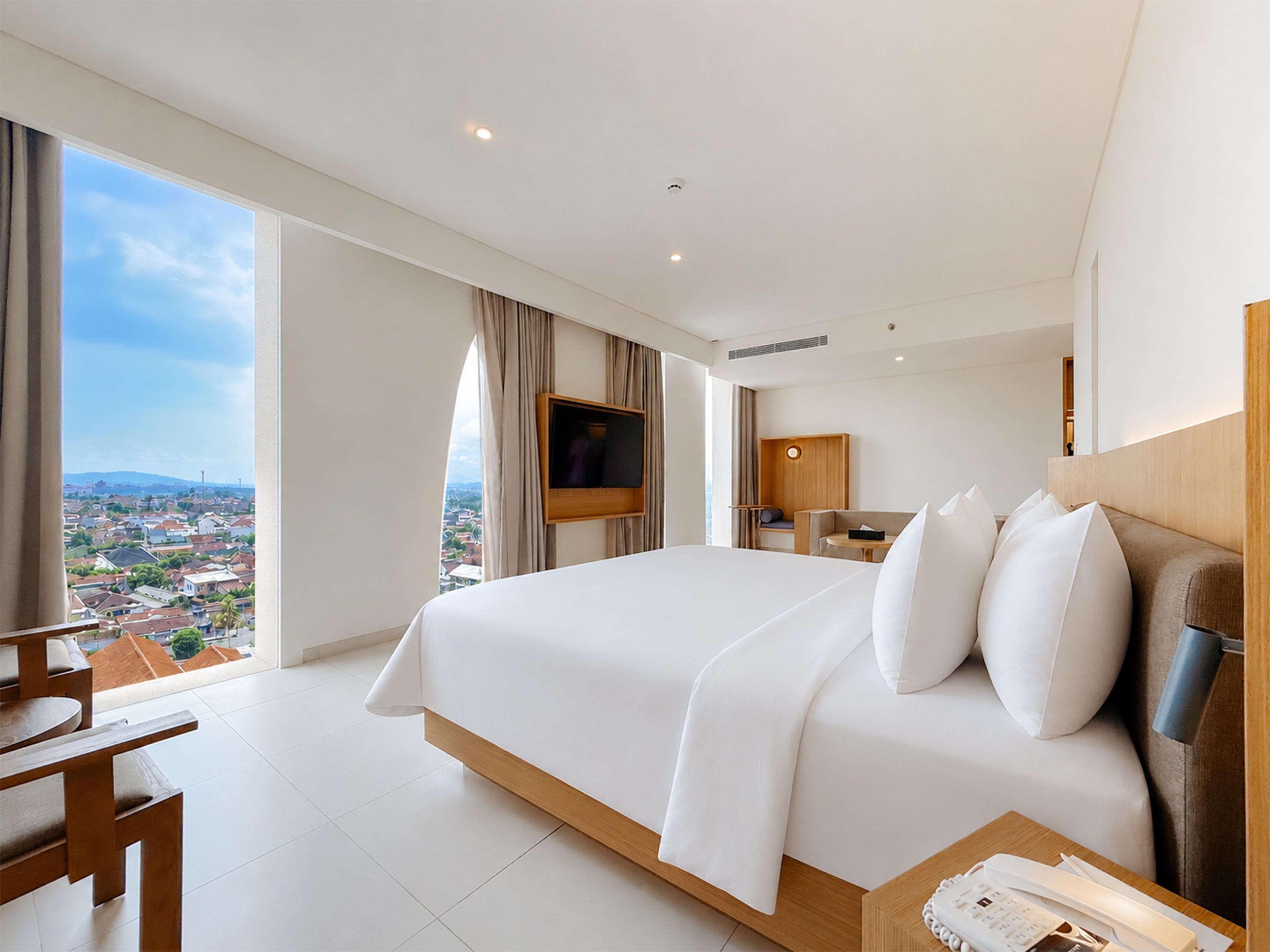 Een hotelkamer met een groot bed, een aan de muur bevestigde televisie, een bureau en uitzicht op de stad.