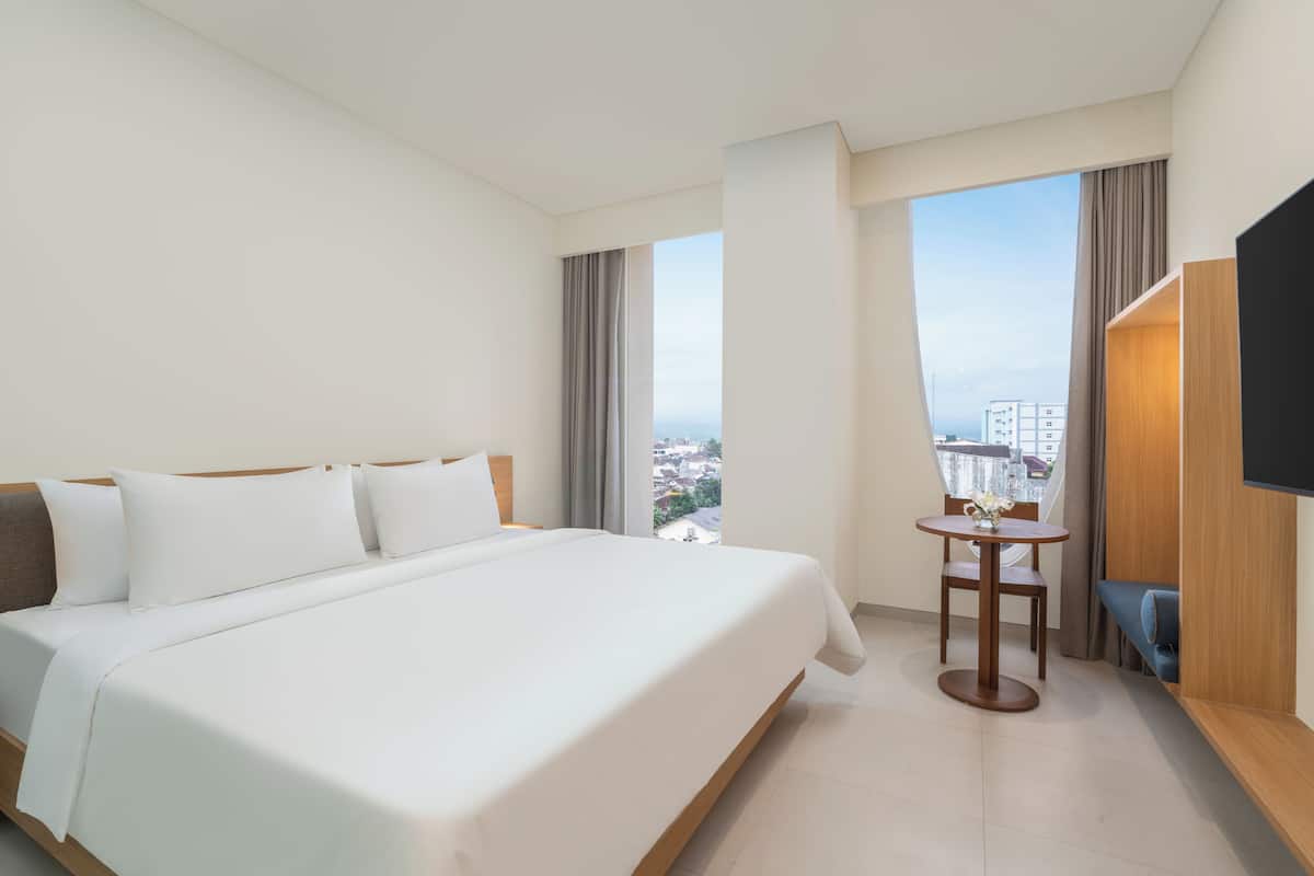 Habitación de hotel con una cama grande, una mesita, televisión y vistas a la ciudad.