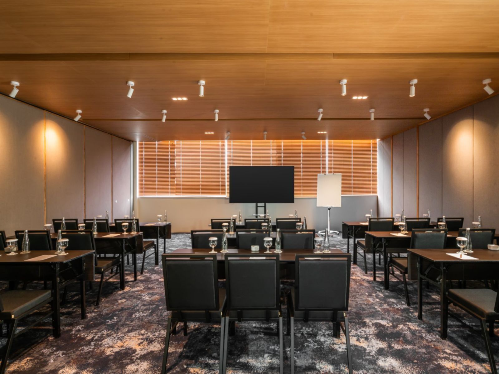Une salle de conférence équipée de plusieurs tables, de chaises, d’un grand écran et d’un projecteur.