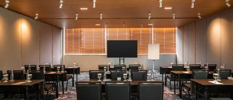 Un salón de conferencias con varias mesas, sillas, una pantalla grande y un proyector.