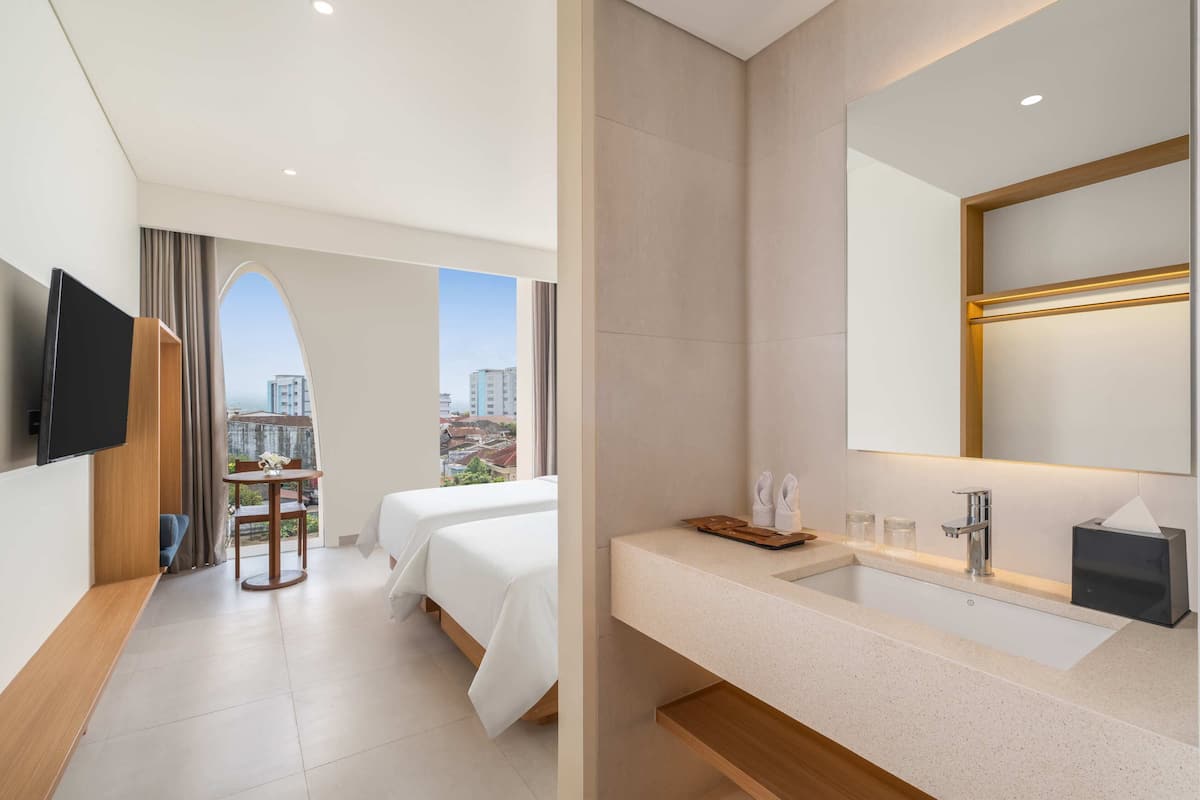 Habitación de hotel con cama, televisión, escritorio y baño con lavamanos y espejo.