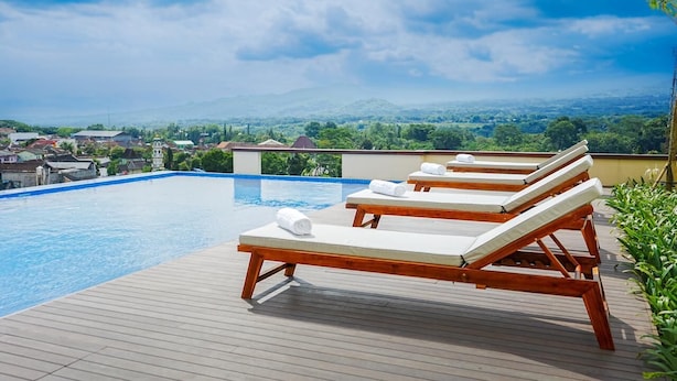 Piscina en la azotea con tumbonas de madera y vistas a un paisaje urbano.