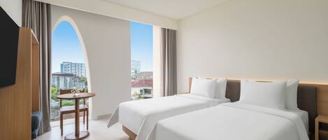 A hotel room with two beds, a TV, a small table with a chair, and a view of the city.