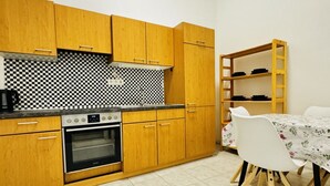 Een keuken met houten kastjes, een geruit achterwand, een fornuis en een eethoek met een tafel en stoelen.