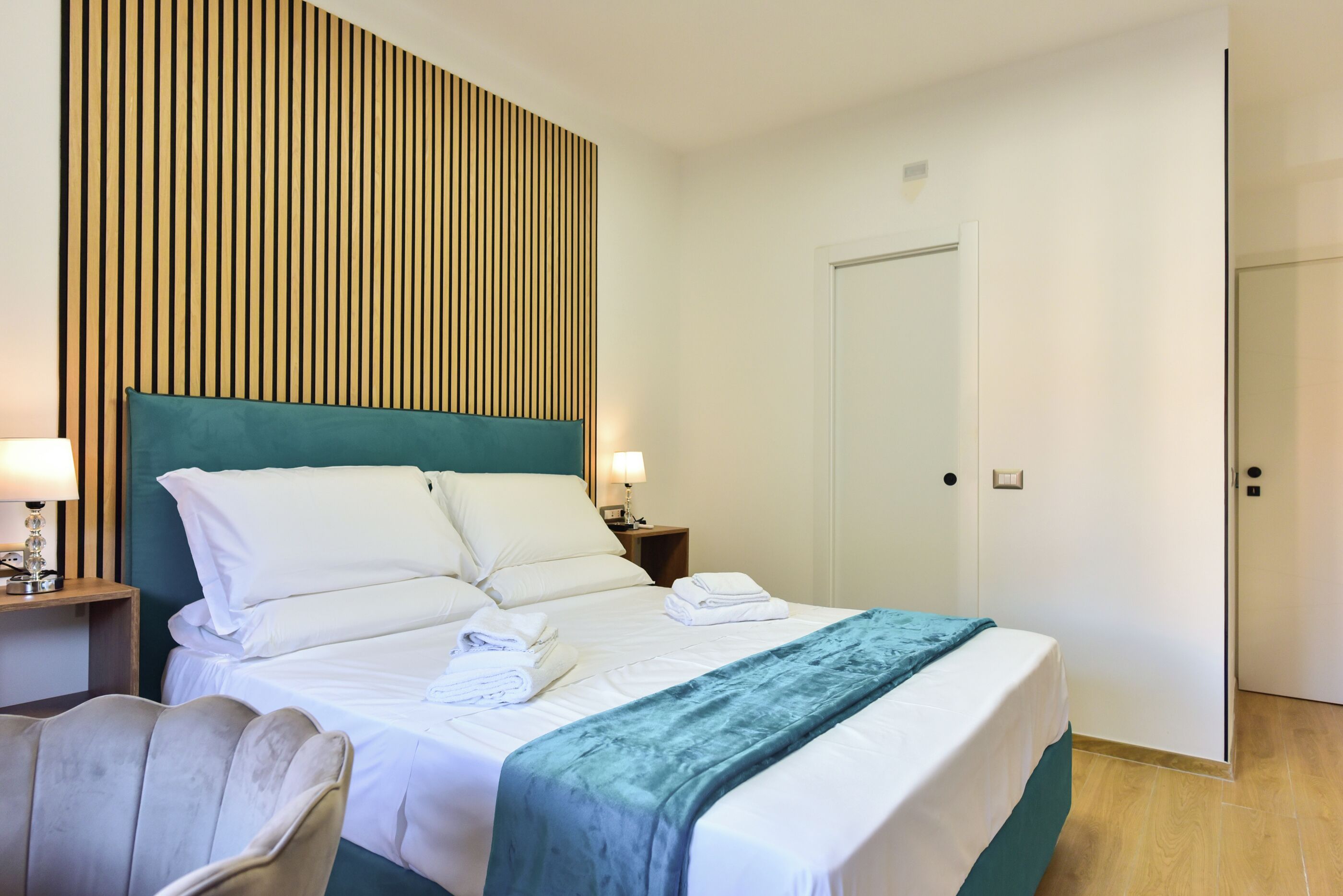 Una habitación de hotel con cama, mesita de noche, una silla y una puerta.