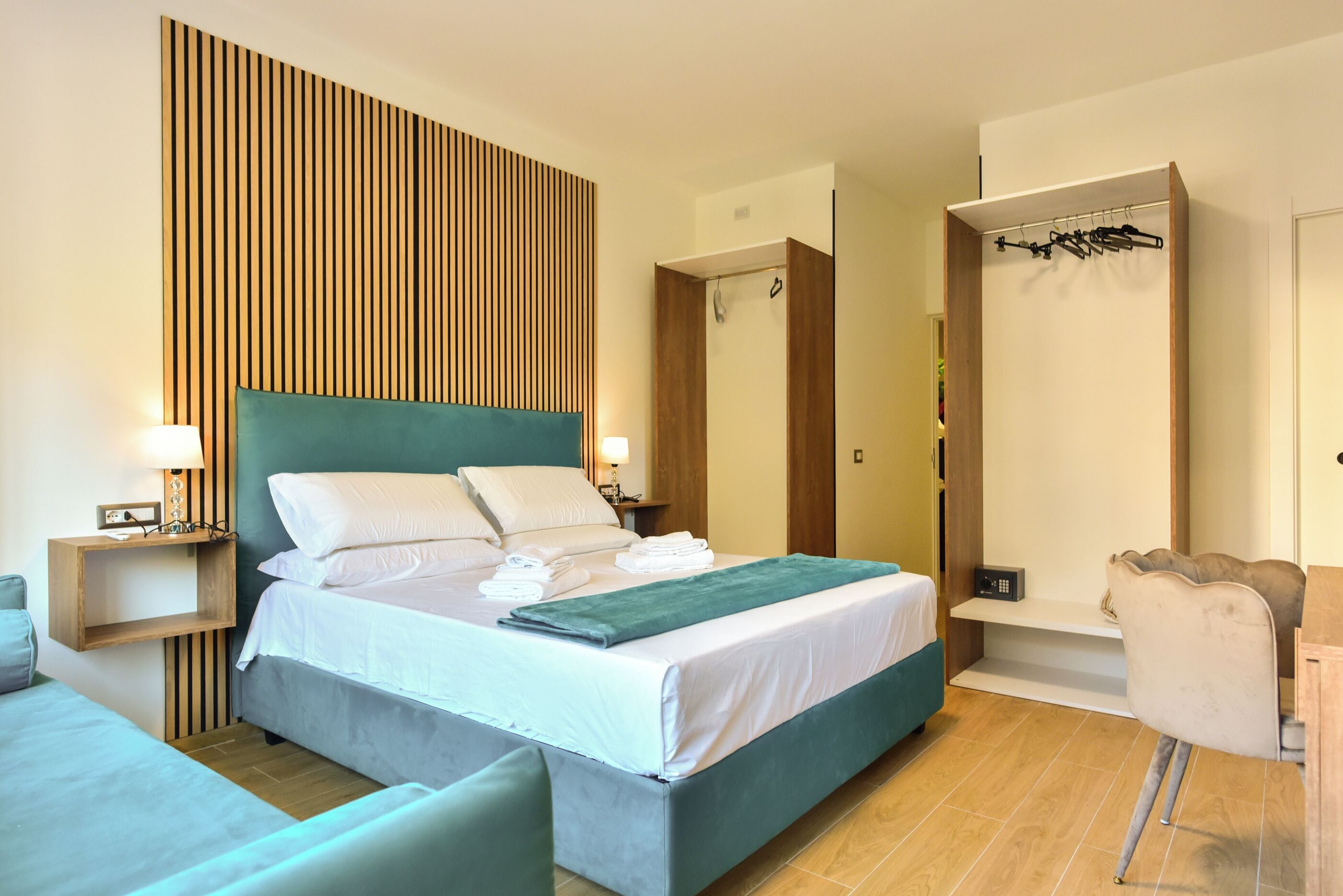 Ein modernes Hotelzimmer mit einem großen Bett, einem Lattenrost, einem eingebauten Kleiderschrank und einer Sitzecke mit einem Sessel.