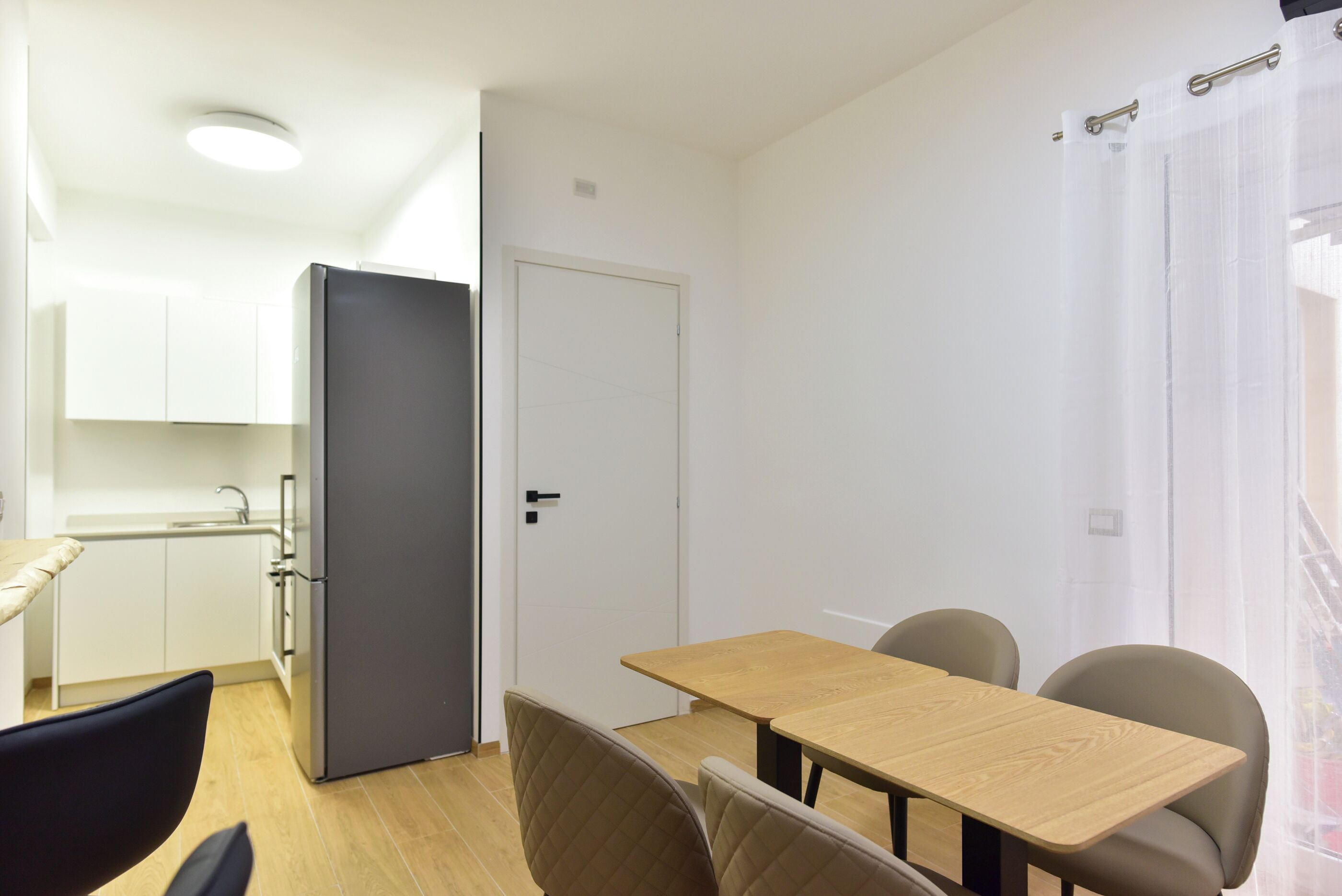 Una cocina compacta con armarios blancos, un refrigerador negro y una mesa de comedor de madera con cuatro sillas.