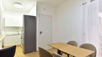 Una cocina compacta con armarios blancos, un refrigerador negro y una mesa de comedor de madera con cuatro sillas.