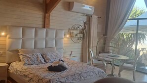 Une chambre avec un grand lit, un miroir rond et un balcon avec des chaises.