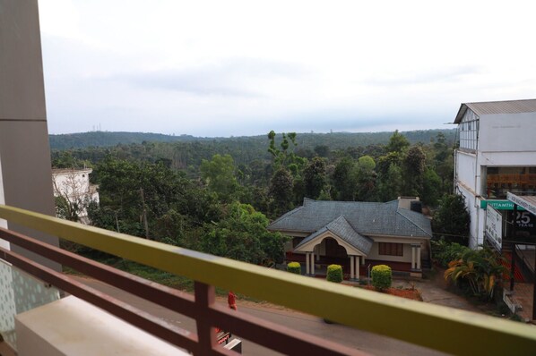 A view from a balcony overlooking a residential area with a house, greenery, and a distant body of water. - Hotel Mountain Hues Thekkady (Udumbanchola)