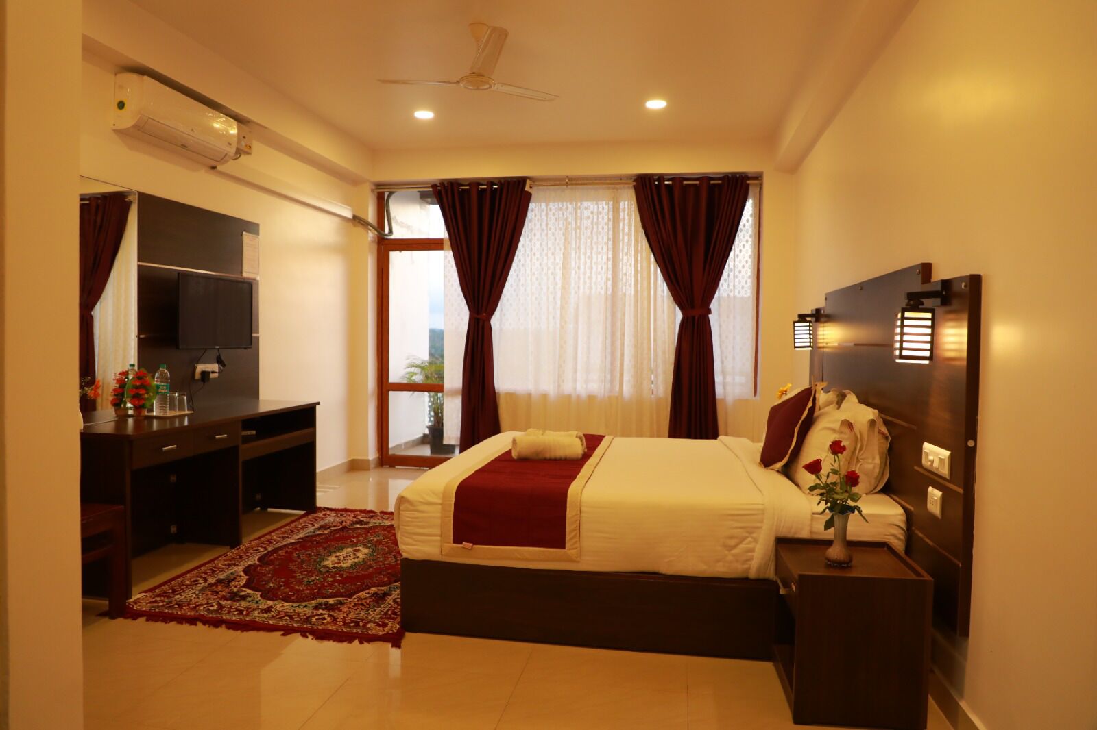 A hotel room with a bed, a desk, a TV, and a window with curtains.