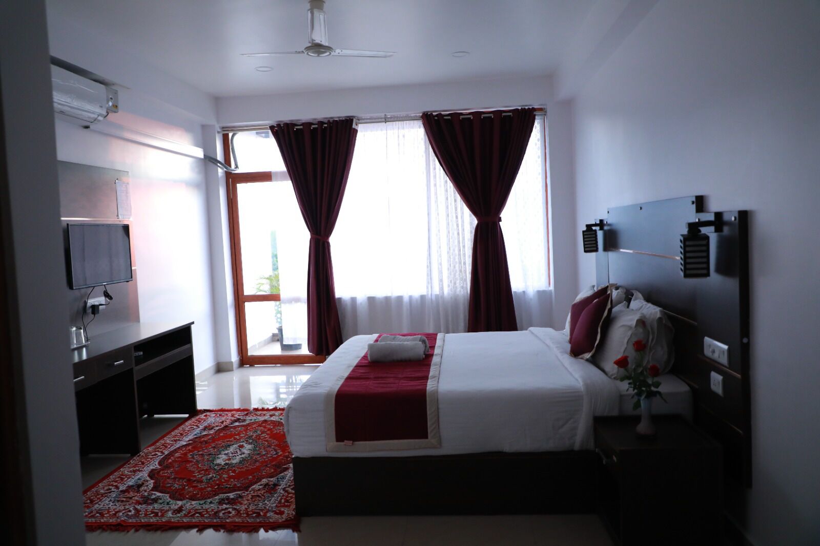 Una habitación de hotel con cama, televisión, escritorio y ventana con cortinas.