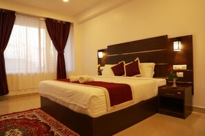 A hotel room with a large bed, dark headboard, bedside lamps, and a red throw blanket. - Hotel Mountain Hues Thekkady (Udumbanchola)
