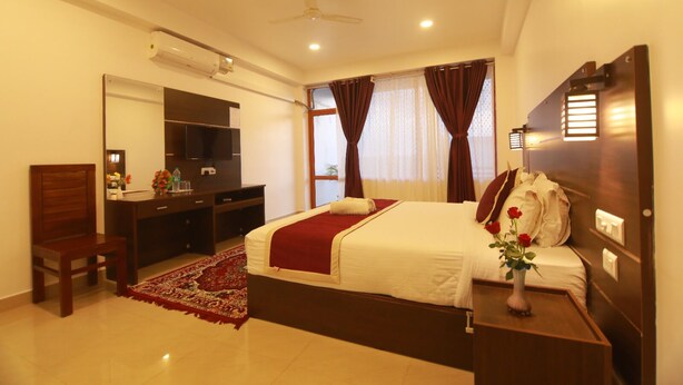 A hotel room with a bed, a desk, a chair, a TV, and a window with curtains. - Hotel Mountain Hues Thekkady (Udumbanchola)